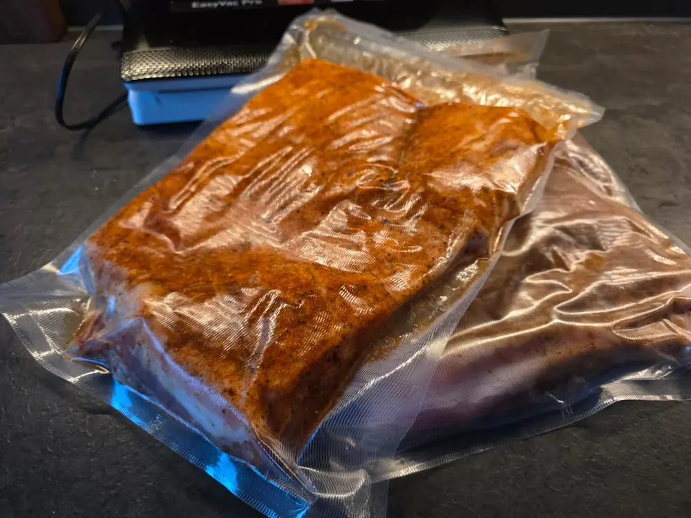 Twee vacuumzakken met gepekeld buikspek naast een vacuummachine